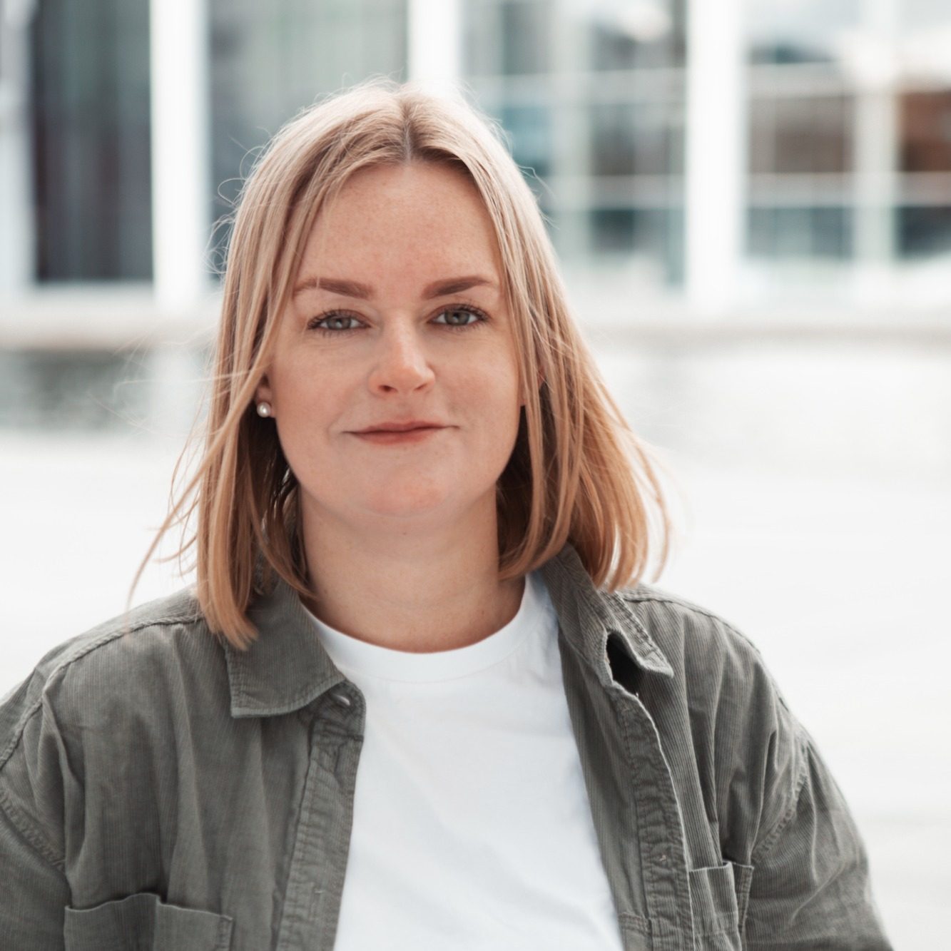 Susann Herzog, systemische Coachin in Berlin“ Junge Frau mit blonden Haaren und lässiger Kleidung steht vor einer modernen Glasfassade.